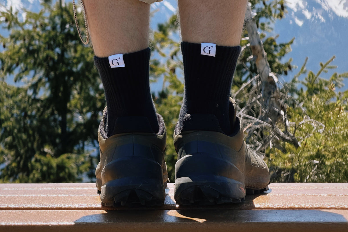 Person wearing black socks with a logo, standing on a wooden platform with mountains in the background.
