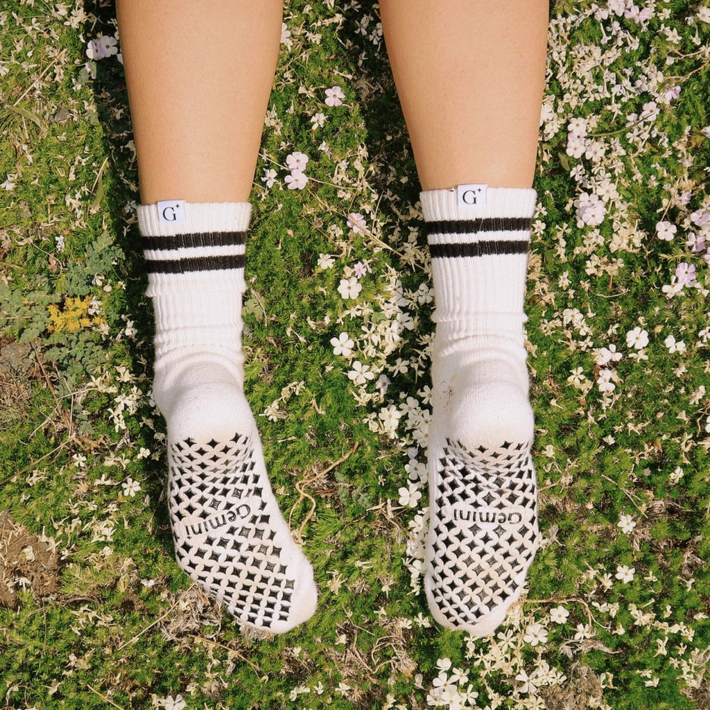 White socks with black stripes on a person standing on a grassy and flower-covered ground.