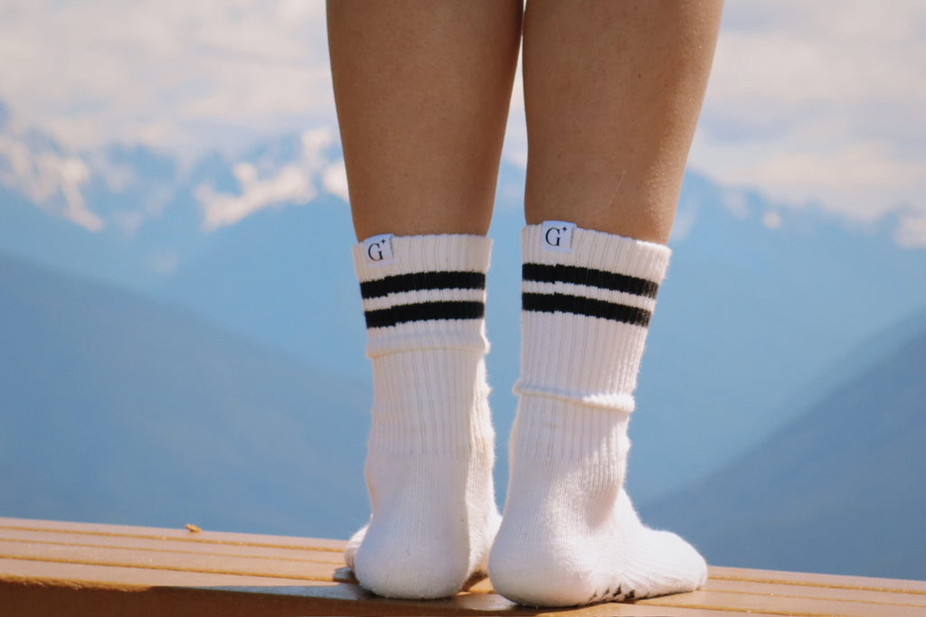 White socks with black stripes worn by a person standing on a wooden platform with a mountainous background.