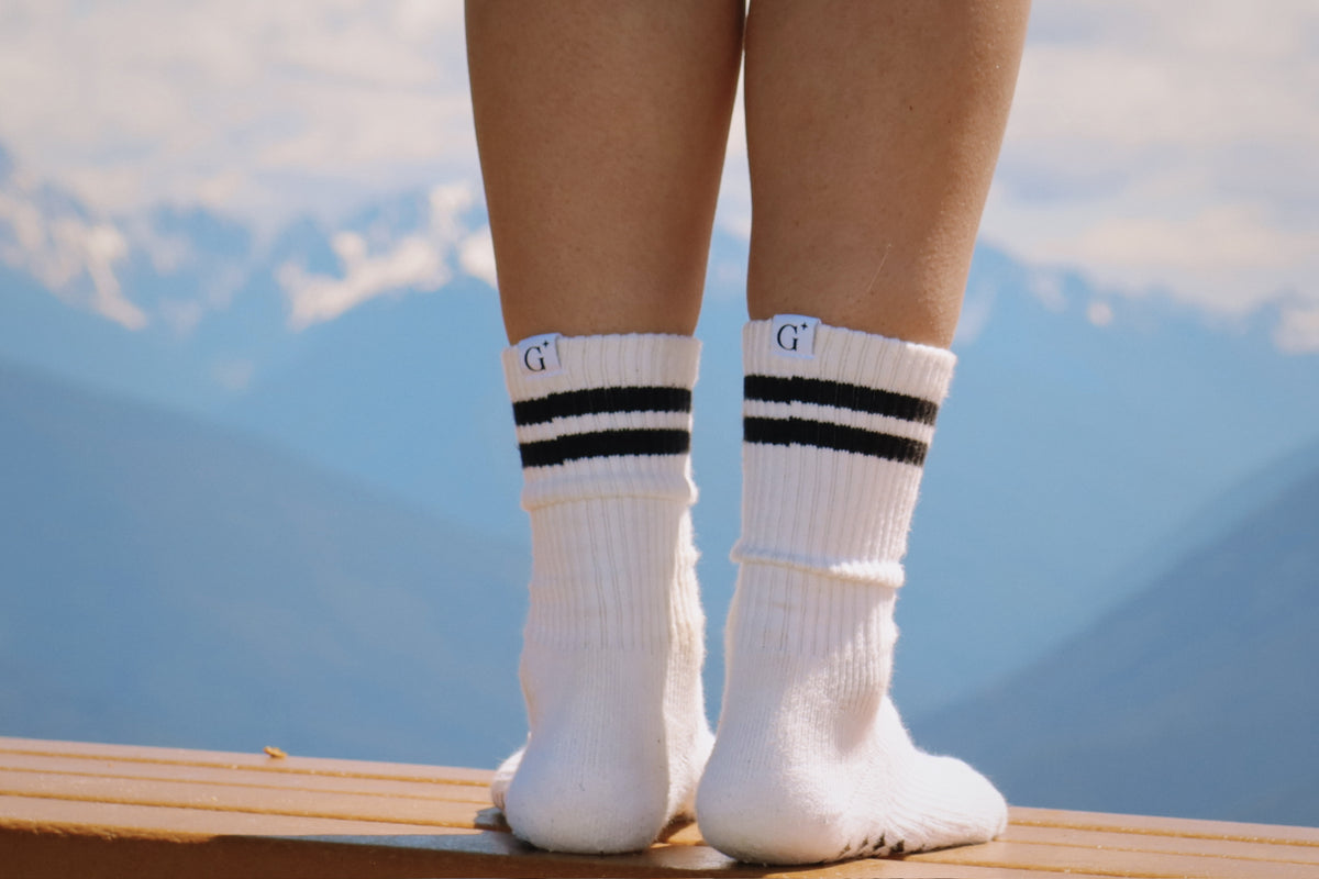 White socks with black stripes worn by a person standing on a wooden platform with a mountainous background.
