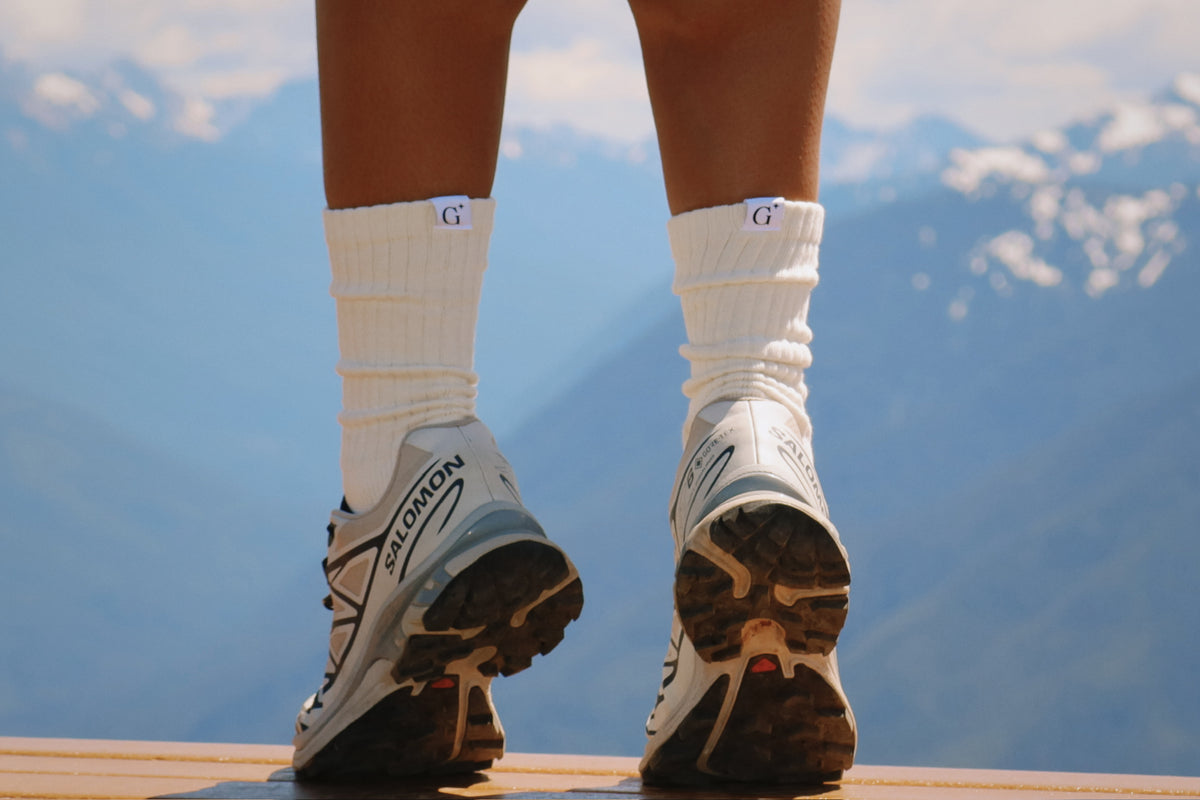 Person wearing white sneakers and socks with a mountainous background