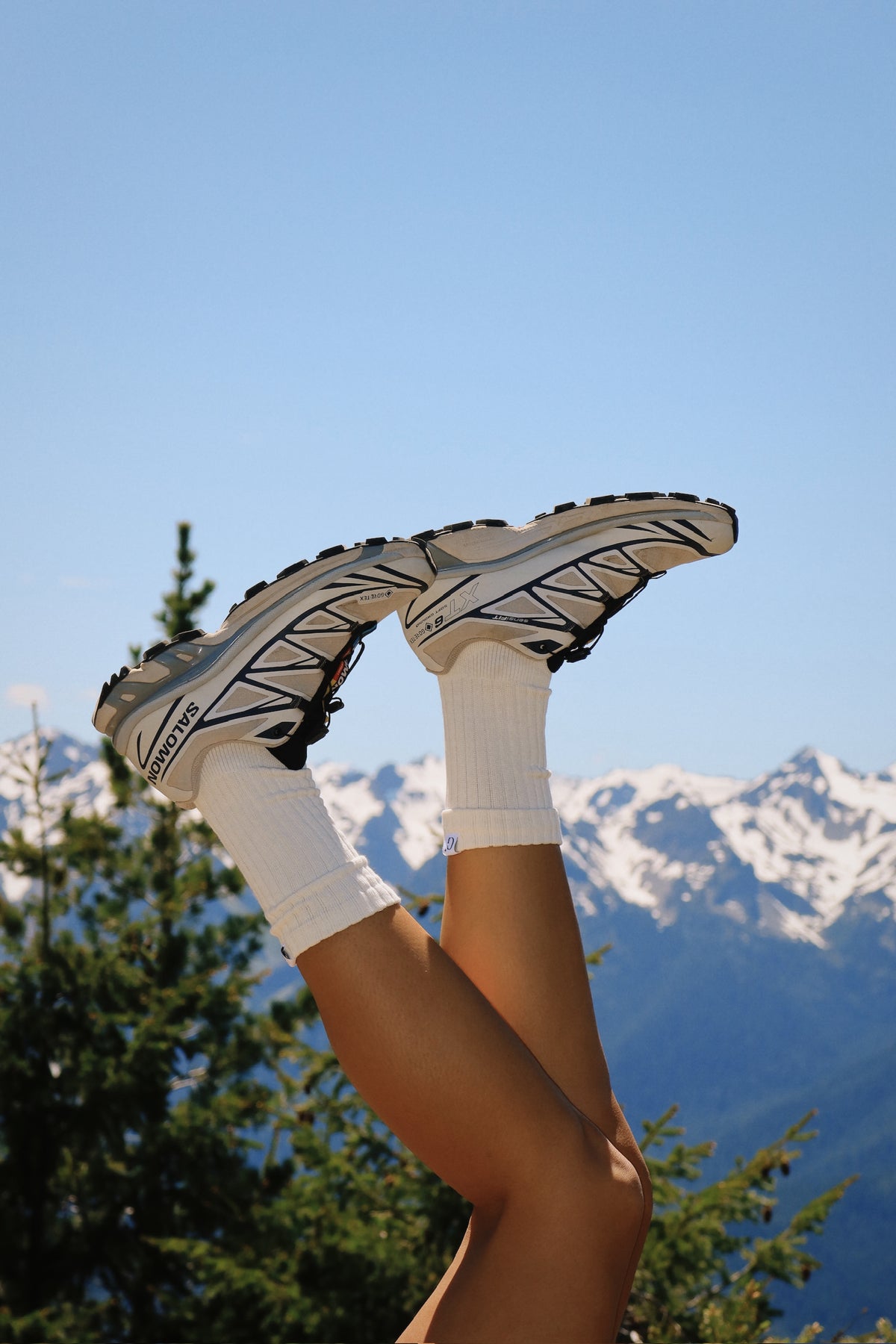 Person wearing white sneakers with black soles against a mountainous landscape